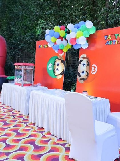An outdoor activity station for a Super Mario party. The setup includes a tattoo artist booth with Mario-themed branding and a popcorn machine to keep the little gamers energized.