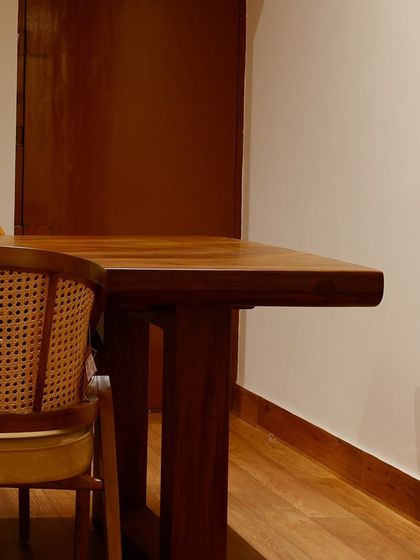 A side view of a live-edge teak dining table paired with a rattan chair. The rich wood grain and natural textures are central to my design philosophy.