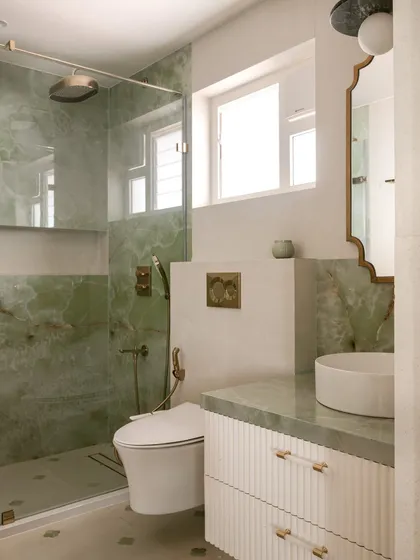 This bathroom for a client's daughter features soothing green onyx on the walls and countertop. We designed a custom floating vanity with a reeded front and acrylic and brass handles for a look that is fresh and modern.