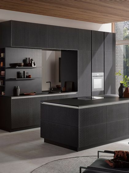 The award-winning wickerwork design shown in a black oak finish, paired with a sleek, handleless island for a modern yet timeless kitchen.