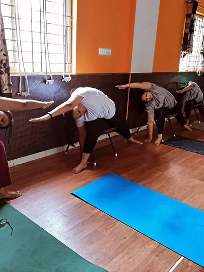 Participants perform a deep side-body stretch while seated on chairs. This pose is excellent for releasing tension in the shoulders and back, common issues for office workers.
