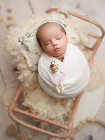 One month of pure wonder. This little one is peacefully asleep on a miniature sleigh prop, holding a tiny ballerina doll, creating a whimsical and sweet memory.