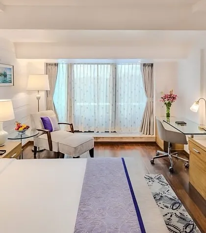 The bedroom area of the Taj Vivanta Goa suite, featuring a clean, modern aesthetic with pops of purple. The design includes a dedicated workspace and a comfortable lounge chair, catering to both leisure and business travelers.