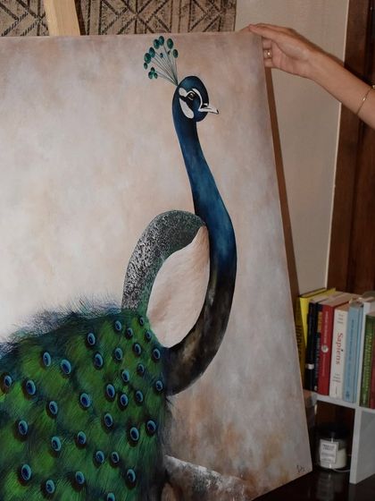 A close-up of my hand next to the finished peacock, highlighting the fine details on the bird's neck and crown. This shows the level of intricate work involved in my wildlife paintings.