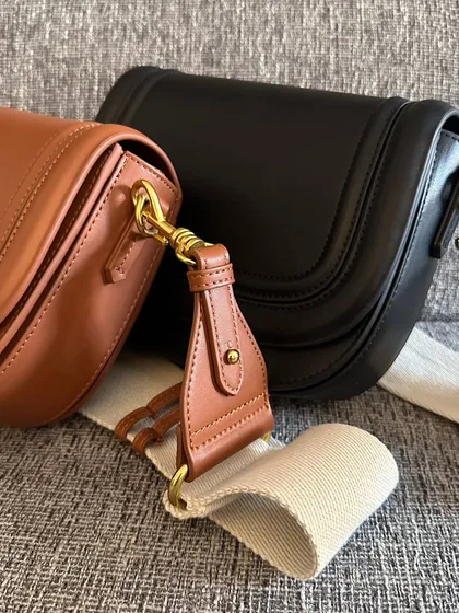 A detailed shot focusing on the hardware and strap of the Noble bag. The brass clasp and leather details on the fabric strap show the attention to quality.