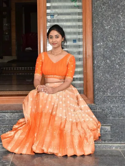 This client is wearing a beautiful orange half-saree. The skirt is made from a Kanchivaram saree, paired with a simple, matching embroidered blouse.