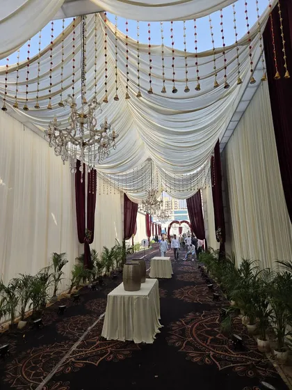 The entrance to a beautiful wedding event we catered. The elegant pathway, lined with plants and adorned with draped ceilings and chandeliers, sets a luxurious tone for the celebration from the moment guests arrive.