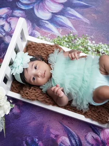 This two-month-old is looking angelic in a mint green outfit, resting in a miniature white crib against a dreamy floral backdrop.