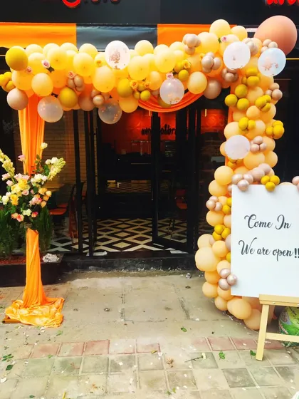 Welcoming customers with a vibrant balloon arch for a store's grand opening. This bright orange and gold balloon arrangement frames the entrance perfectly, creating an inviting and celebratory atmosphere to attract attention and mark the special occasion.