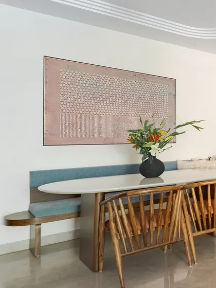 In this open-concept dining area, a bench against the wall creates a cozy, café-like vibe. The bespoke wooden chairs reflect the Wabi-Sabi aesthetic, and the artwork connects the space to the adjacent living area.