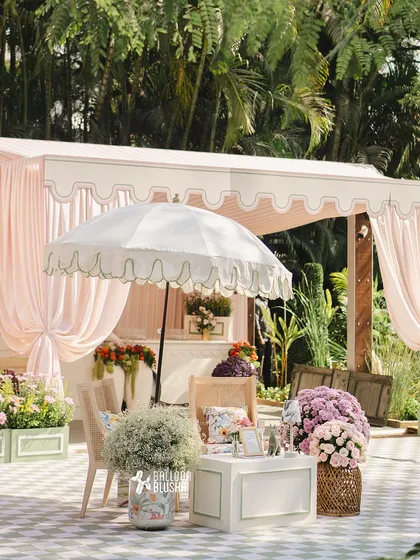 An elegant outdoor lounge area with a scalloped-edge umbrella, pink drapery, and comfortable seating with floral cushions.