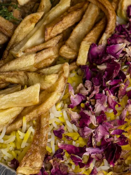 A vibrant close-up of the biryani garnish, featuring crispy golden fries, fragrant saffron rice, and delicate dried rose petals.