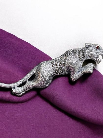 A stunning silver brooch in the shape of a leaping panther. The body is detailed with marcasite, and a tiny red stone forms the eye.