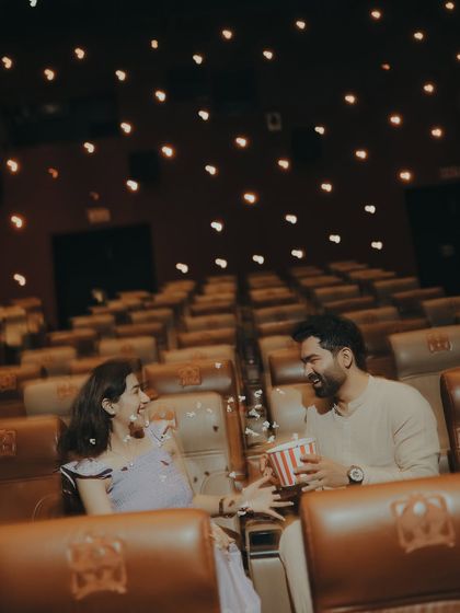 A playful moment sharing popcorn in a theatre. This shot adds a fun, candid element to the cinematic pre-wedding shoot, showing the couple's relaxed chemistry.