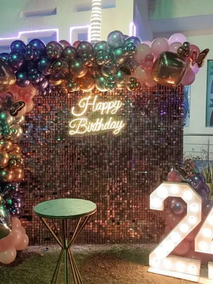 An outdoor setup for a 24th birthday, featuring a bronze sequin wall with a balloon arch and large marquee numbers. This is perfect for an evening party on a terrace or in a garden.