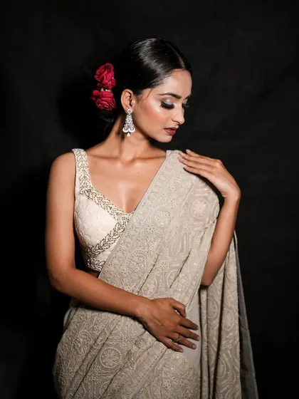 A close-up portrait focusing on the model's serene expression and the details of her festive look, including the red roses in her hair and the intricate embroidery on her blouse.