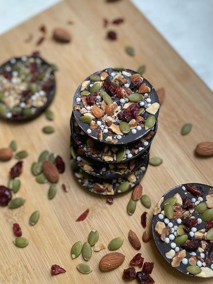 A stack of our crunchy Almond Berry Discs. These dark chocolate treats are loaded with roasted almonds, pumpkin seeds, and tangy dried cranberries for a healthy and delicious bite.
