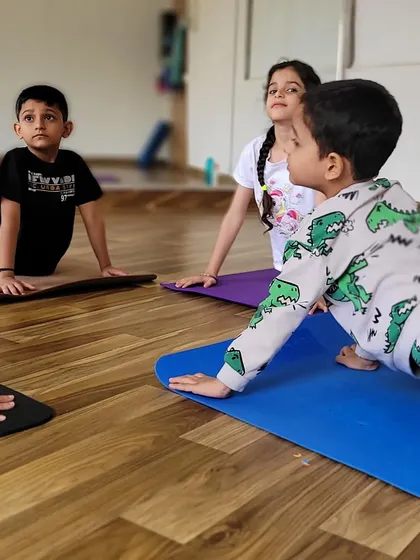 The kids are practicing Bhujangasana, or cobra pose, together. This pose is great for strengthening the spine and opening the chest, and doing it as a group makes it even more fun.