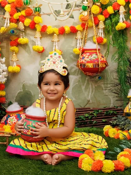 A beautiful portrait of a little girl dressed as Radha, sitting in a festive setup with a big smile.