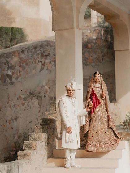 A classic and elegant portrait of the couple on the steps of a palace. Their traditional attire and the historic architecture combine to create a timeless and regal wedding photograph.