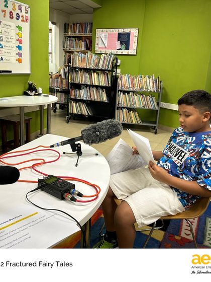 A second-grade student confidently reads his original Fractured Fairytale into the microphone. This project combines writing, storytelling, and technology, giving students a platform to share their creative work with a global audience.