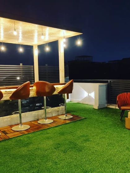 A beautiful terrace featuring a glass room, an elegant bar counter under a pergola, and plenty of green space for relaxation.