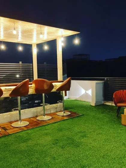 A beautiful terrace featuring a glass room, an elegant bar counter under a pergola, and plenty of green space for relaxation.