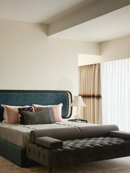 This guest bedroom features a bold blue headboard and a tufted dark grey ottoman. The design is clean and modern, with a focus on comfort and a serene color palette.