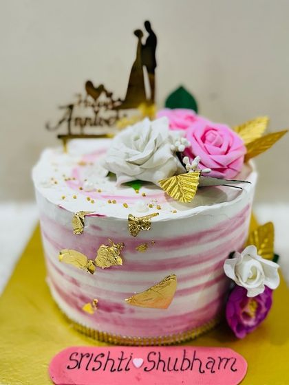A lovely anniversary cake with pink and white watercolor stripes, gold leaf accents, and delicate sugar flowers, celebrating a couple's journey together.