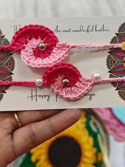 A pair of beautiful pink crochet rakhis, perfect for celebrating the sibling bond. The design is simple yet elegant, with a small pearl detail.