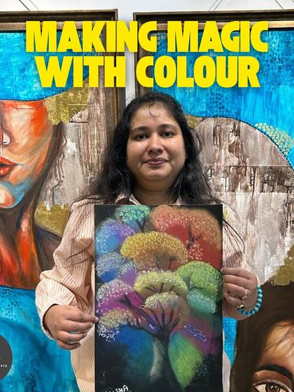 Making magic with color. This student proudly presents her colorful soft pastel drawing, created against a backdrop of other inspiring artworks in the studio.