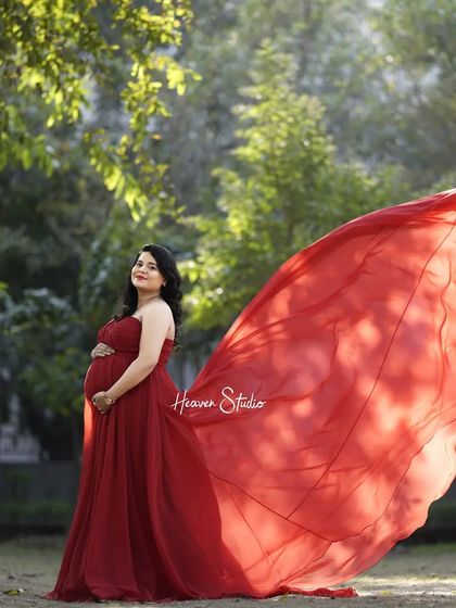 A powerful outdoor portrait. The wind catches the flowing red gown, creating a dramatic and beautiful image that celebrates the strength of motherhood.
