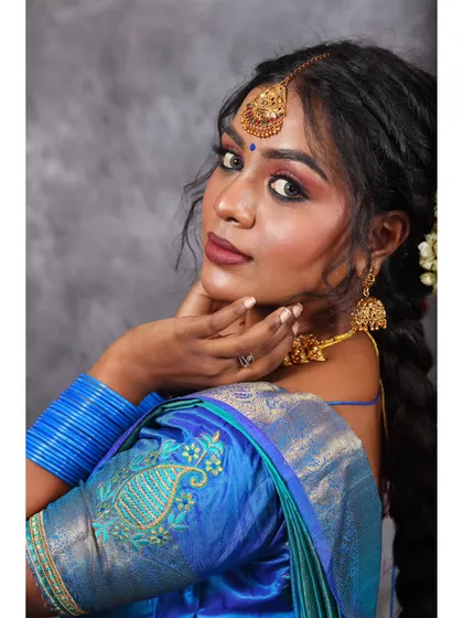 A classic over-the-shoulder pose in a blue silk saree. This angle highlights the detailed embroidery on the sleeve and the traditional braided hairstyle.