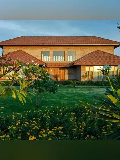 The front facade of the "House with Two Courts" is softened by a vibrant garden. We used a mix of flowering shrubs and leafy plants like frangipani to create a welcoming and colorful entry experience.
