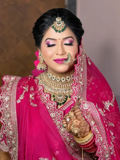 A vibrant bridal look in magenta pink. The heavy Kundan necklace with green accents, paired with a large nath and maang tikka, creates a bold and beautiful statement.