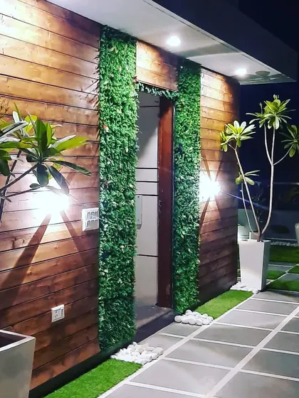 The same glass room at night. The exterior is lit with wall lights and strip lighting, highlighting the wood cladding and vertical gardens.