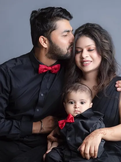 A stylish family portrait in matching black shirts and red bow ties. A father's gentle kiss on his wife's forehead adds a touch of romance.