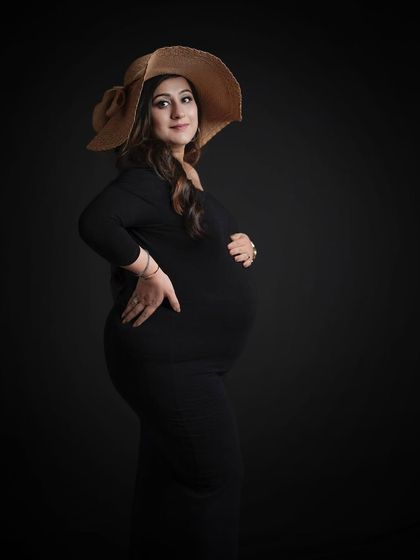 A chic and stylish solo portrait in a classic black dress, accessorized with a wide-brimmed hat for a touch of glamour.