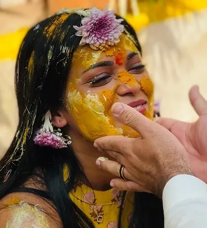 A close-up of the bride's happy expression as her family applies turmeric paste. These are the candid, emotional moments I strive to create the perfect atmosphere for during an intimate Haldi ceremony.