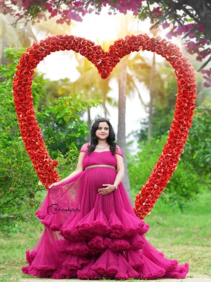A regal portrait of a mother-to-be in a wine-colored ruffled gown and crown, framed by our red floral heart prop.
