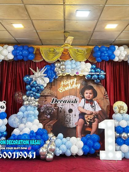 A grand first birthday celebration in a hall with a blue and white theme. The decor features a large balloon arch, a custom photo backdrop, and panda accents for a cute touch.
