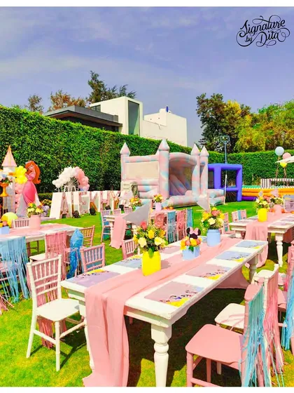 An overview of the kids' dining area at the Disneyland party. The long tables are decorated with pastel pink runners and fringed chair details, with a large bouncy castle visible in the background for fun.