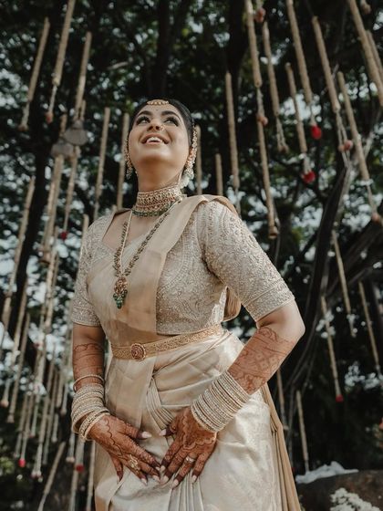 A joyful bride looks up, her face lit with happiness. Her golden saree and heavily worked blouse shimmer in the light, creating a truly magical bridal portrait.