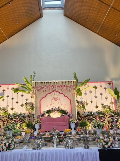 A wider view of the pink floral and banana leaf stage in a hall with a high ceiling.