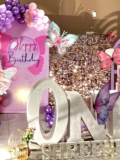 A close-up on the large 'ONE' marquee letters, decorated with beautiful, iridescent butterfly props and set against a rose gold sequin backdrop.