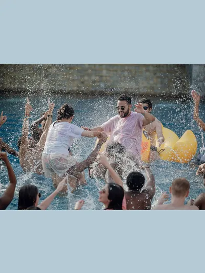 The couple is lifted up by friends in the middle of a chaotic and fun-filled pool party celebration.