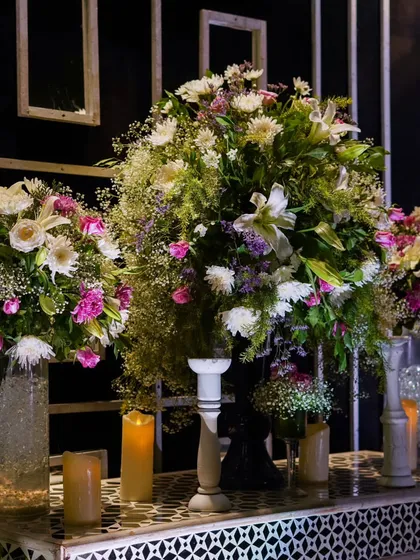 An opulent display of large floral arrangements in white and purple hues, placed on intricate white stands, adding a touch of softness to the dramatic black-and-white decor.