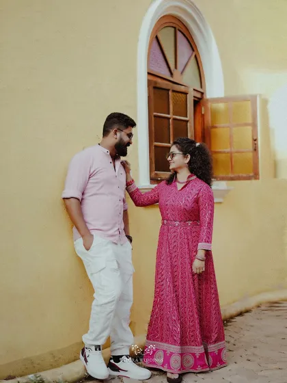 The couple posing by a yellow wall and an arched window, their outfits providing a beautiful color contrast.