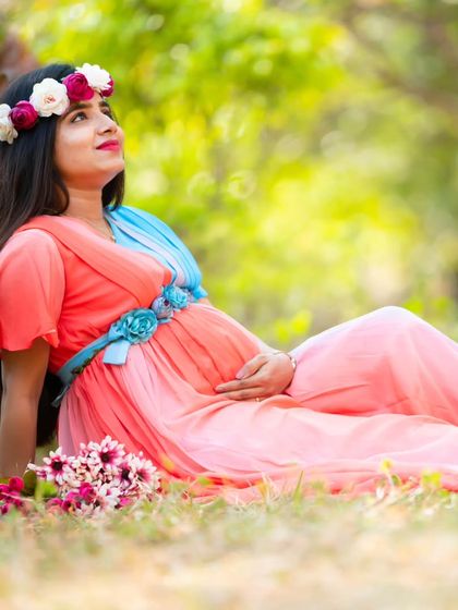 A dreamy outdoor portrait. The mom-to-be lies peacefully in the grass in a colorful gown, surrounded by flowers, creating a serene and beautiful image.