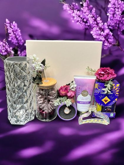 A luxurious lavender-themed gift hamper for a sister. This set includes a crystal-cut vase, a glass tumbler, body wash, chocolates, and hair accessories, all beautifully arranged.